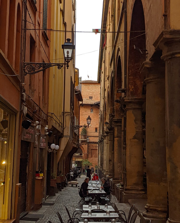 Restaurant tables set out along a typically Bolognese street