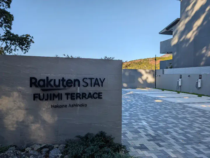 The entrance to Rakuten Stay Fujimi Terrace. The apartment complex name is on a stone plaque, and there are electric car parking spaces in the background.