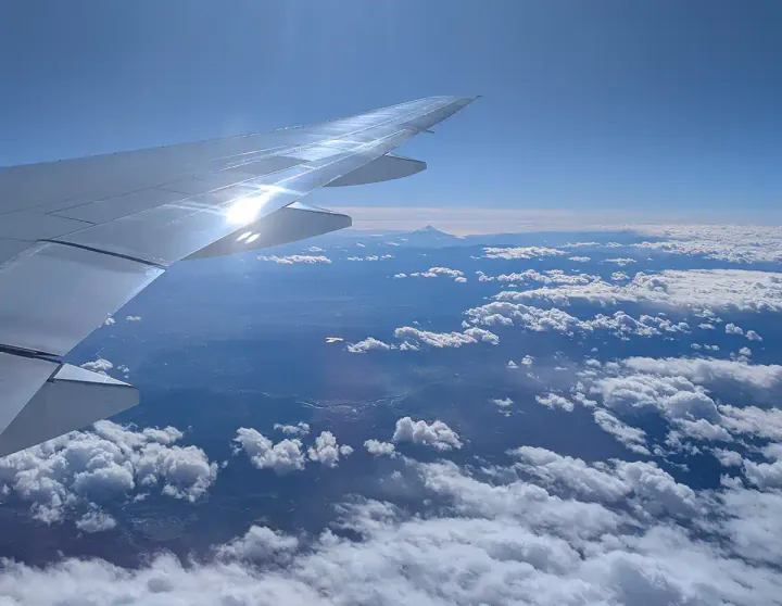 A plane wing flying in the sky, with the tip of Mount Fuji poking out in the distance