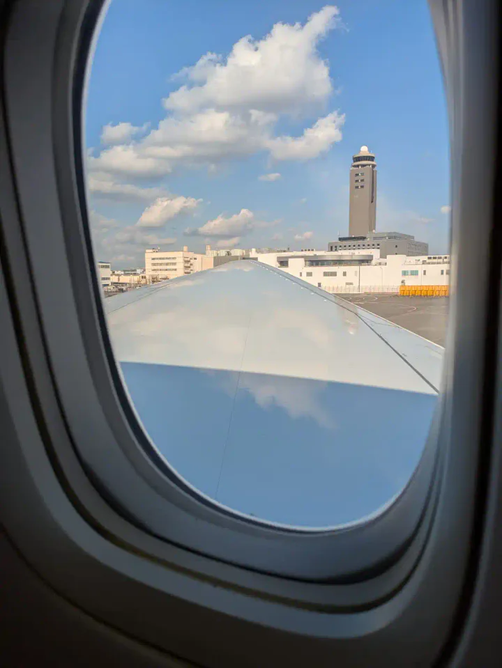 Leaving Tokyo Narita airport. Through a plane window you can see a plane wing and the air traffic control beyond.