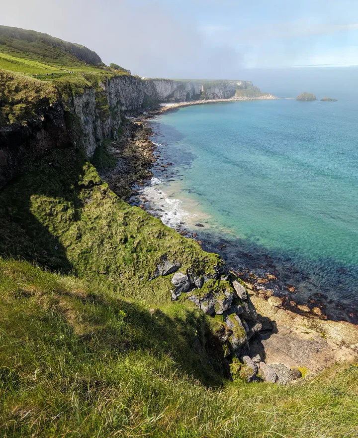 Green undulating cliffs above a beautiful turquoise sea, with waves crashing at their base