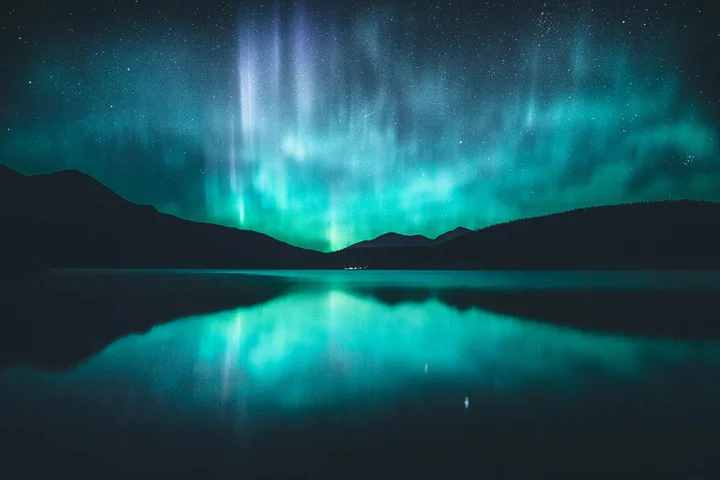 Bright green and blue northern lights reflecting in a lake in Jasper National Park