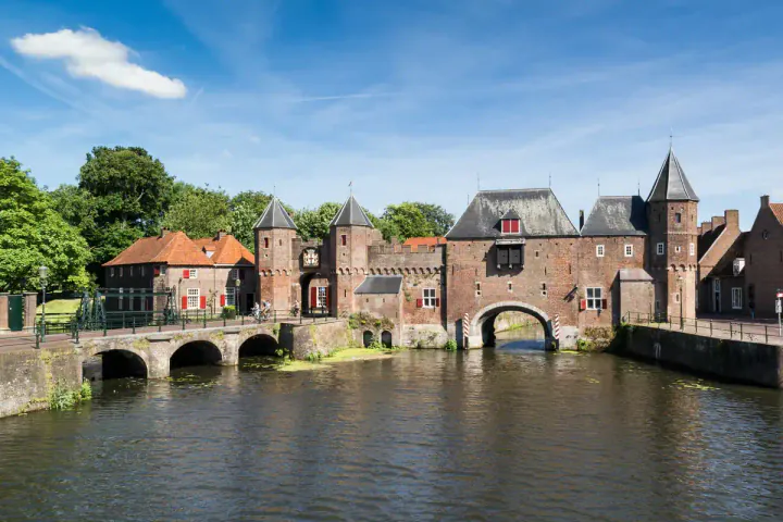 A wide medieval gate with turrets, spanning both a road and a waterway.