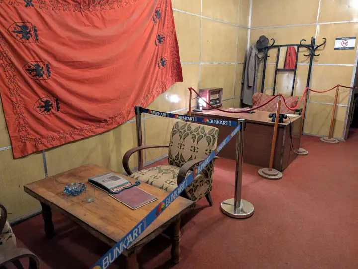 Enver Hoxha's office at what is now Bunk'Art 1. A narrow room has a desk and seating area. There's a large Albanian flag hung on the wall.