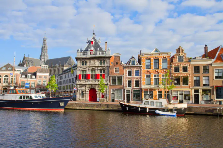 A row of colourful medieval buildings along a river, with boats in front