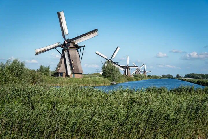 A row of traditional windmills along a waterway in a flat rural landscape