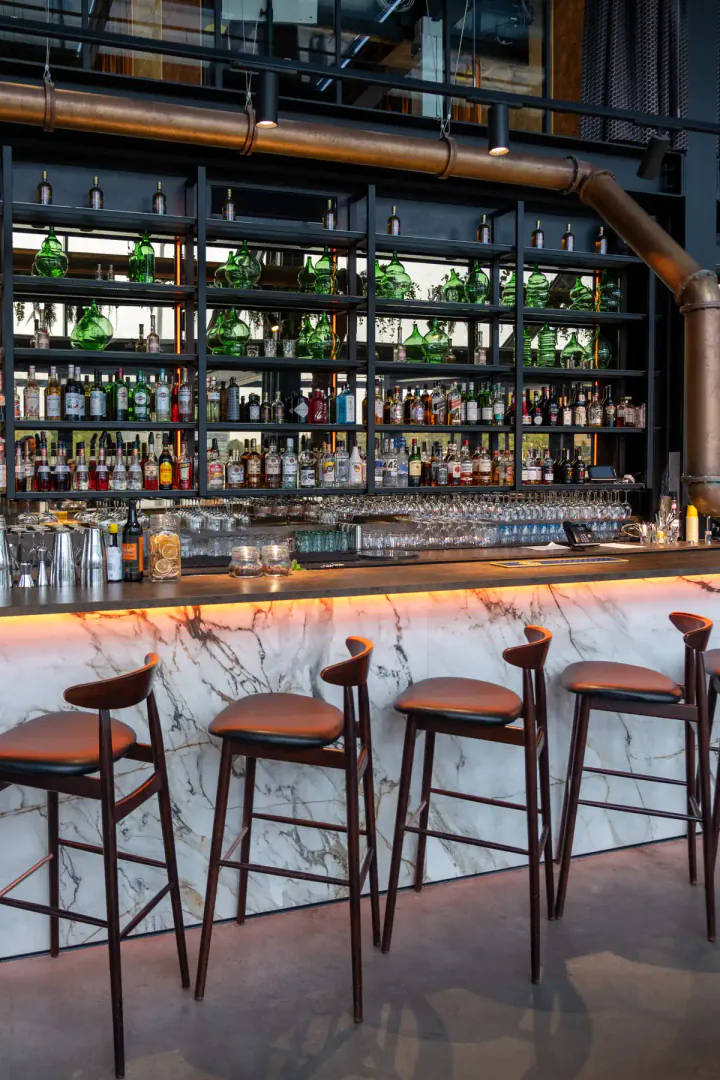 A hotel bar, with tall seats and lots of high shelves with a wide range of drinks