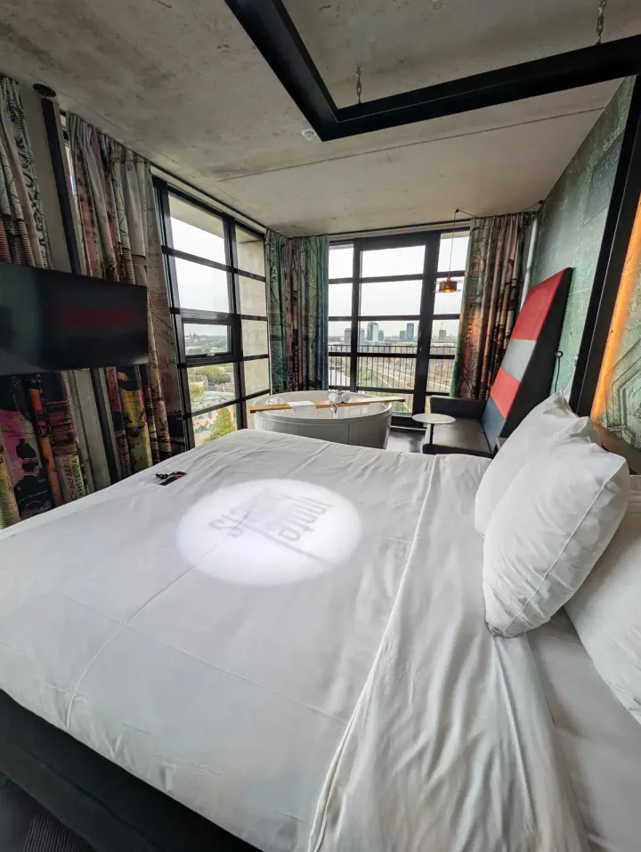 A luxurious hotel rom with a huge bed, two corner floor to ceiling windows and a whirlpool bath overlooking the view
