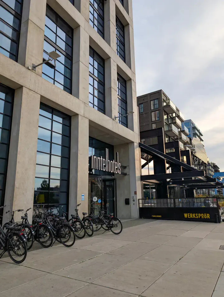 The entrance to the Inntel Hotels Landmark hotel in Amsterdam. A tall, modern building with bikes for rent outside and more modern, industrial-inspired buildings next door.