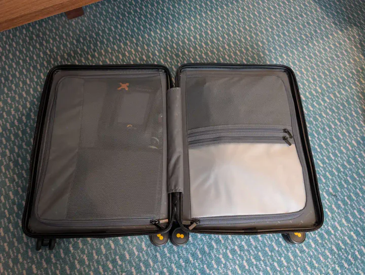 A suitcase open on the floor, showing the neat zip covers separating the compartments