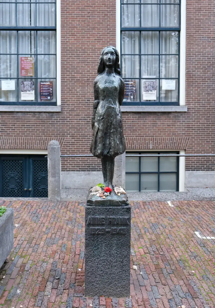A small statue of Anne Frank beside the Westerkerk in Amsterdam. Flowers have been left on the statue's plinth.