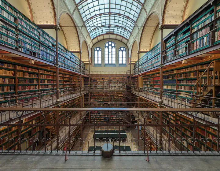 A beautiful old library, with wooden shelves, galleries to walk along in front of the bookshelves and a glazed, arched roof.