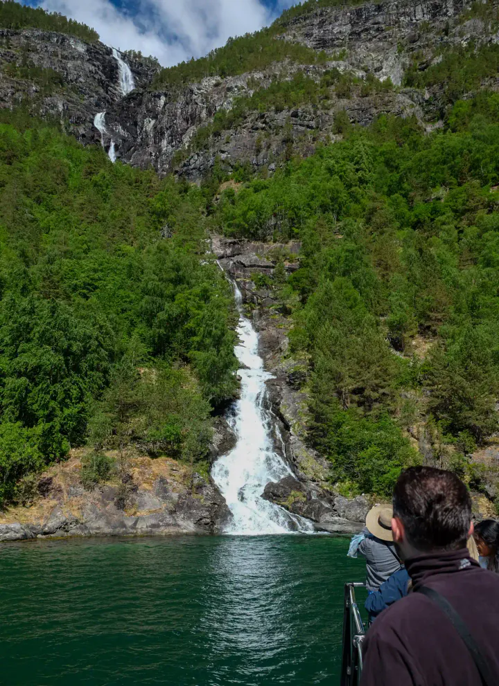 A tall waterfall crashing into the waters of the fjord