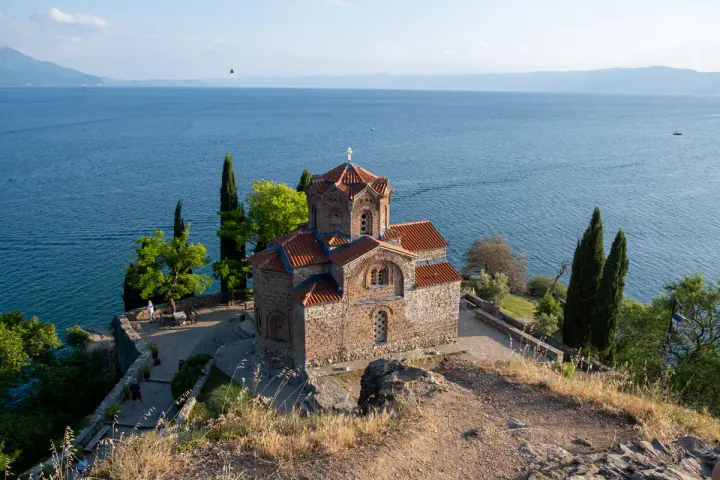 A Byzantine brick church with a red tiled roof set on a clifftop above a lake