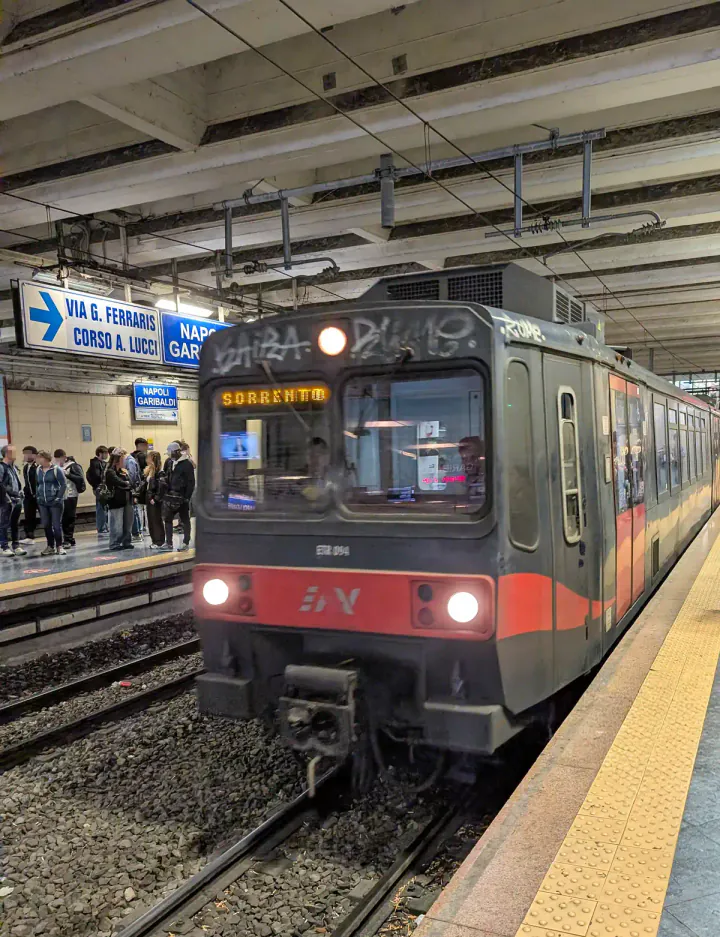 A Circumvesuviana train arriving at Napoli Garibaldi station. The train is dirty and moving very fast. It has a sign saying Sorrento on the front.