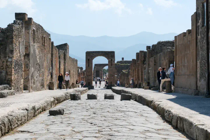 A street in Pompeii, with pavements, large stones for crossing the road and an arch in the background