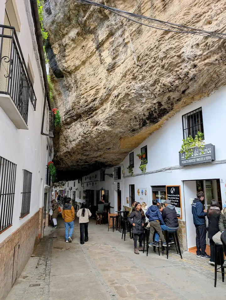 C. Cuevas de la Sombra in Setenil de las Bodegas. A normal-looking street with white houses and a bar has a giant rock for a roof cutting right across it.