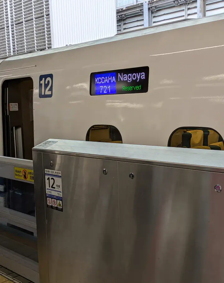 A Shinkhansen train at Tokyo Station, showing the train's destination (Nagoya) and the train name and number (Kodama 721) on the coach display