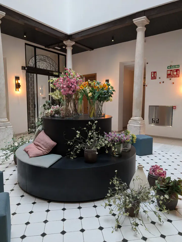 A circular seat in a large room with columns and a black and white tiled floor. There are vases of flowers everywhere.