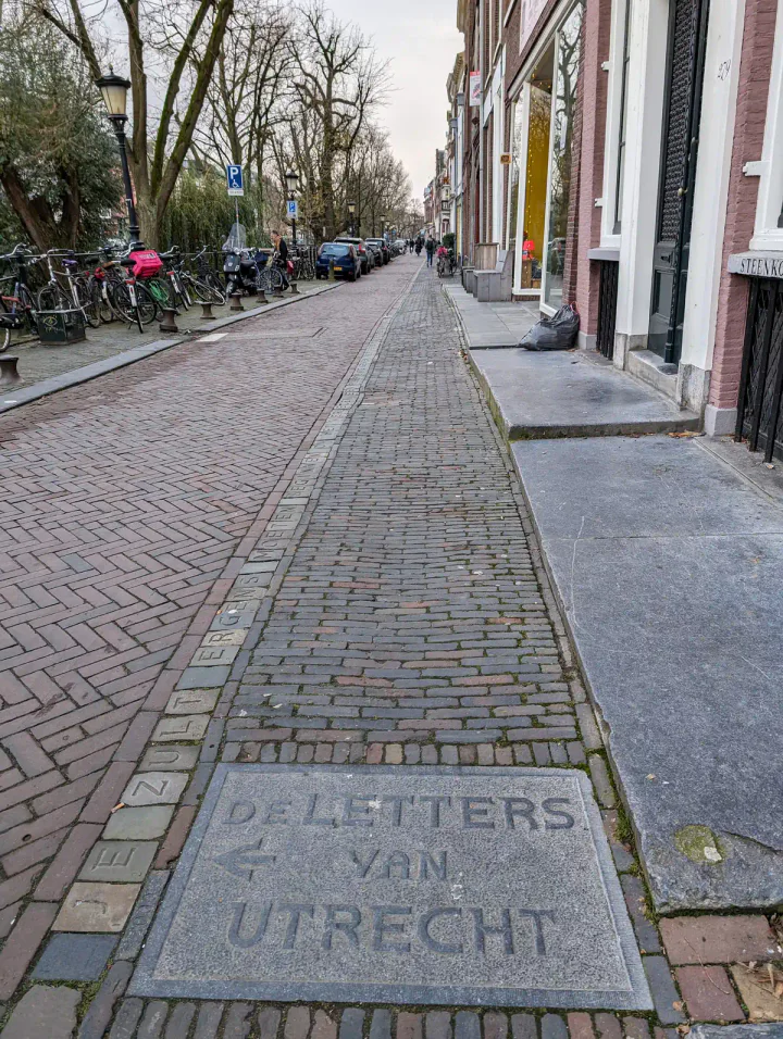 A street running beside a canal, with letters carved into stone running along the pavement