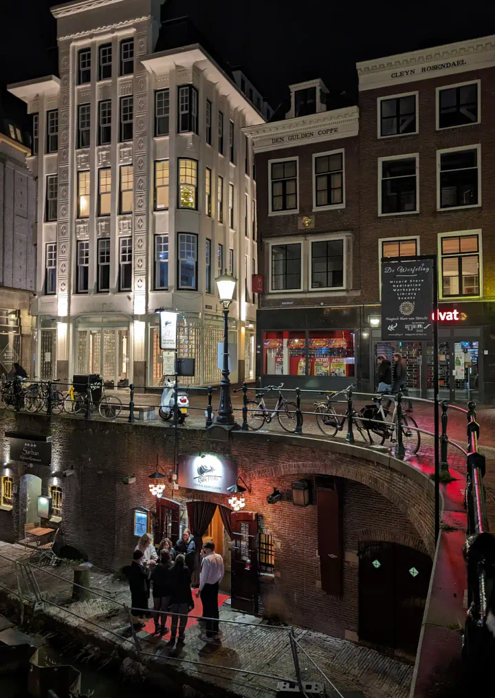 People standing outside a restaurant beside a canal. The main street level is above.