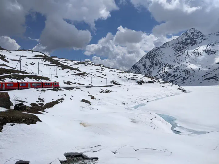 A red Bernina Line train travelling through snowy mountains on the way from Switzerland to Italy