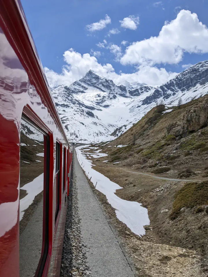 A red Bernina line train travelling through snowy mountains on the way from Switzerland to Italy