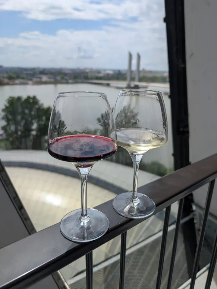 Two glasses of wine, one red, one white, on a railing overlooking a river