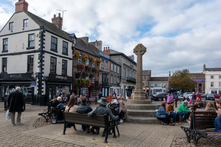 A busy market place in a small town with a stone market cross
