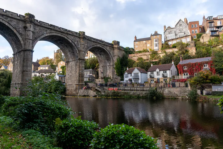A graceful railway viaduct crossing a river in a deep gorge. There are old stone houses on the other side of the river.