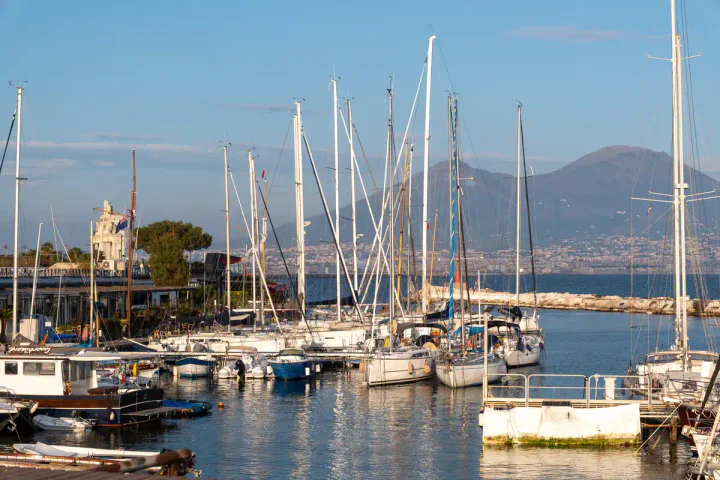 A harbour with sailing boats, with Mount Vesuvius in the background