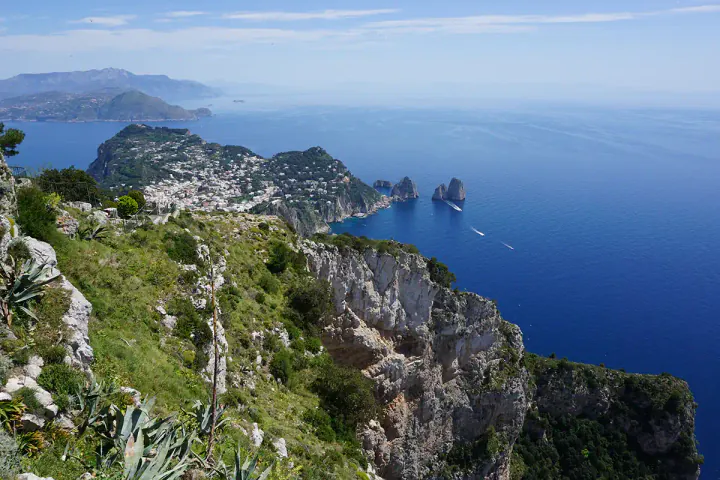 A view from the top of Monte Solaro on Capri, looking out over rocky cliffs towards a deep blue sea