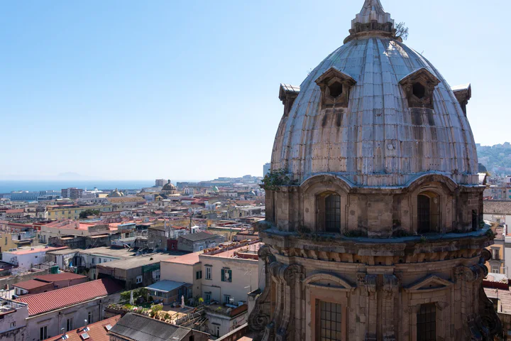 A large church dome and a view over the rooftops of Naples towards the sea