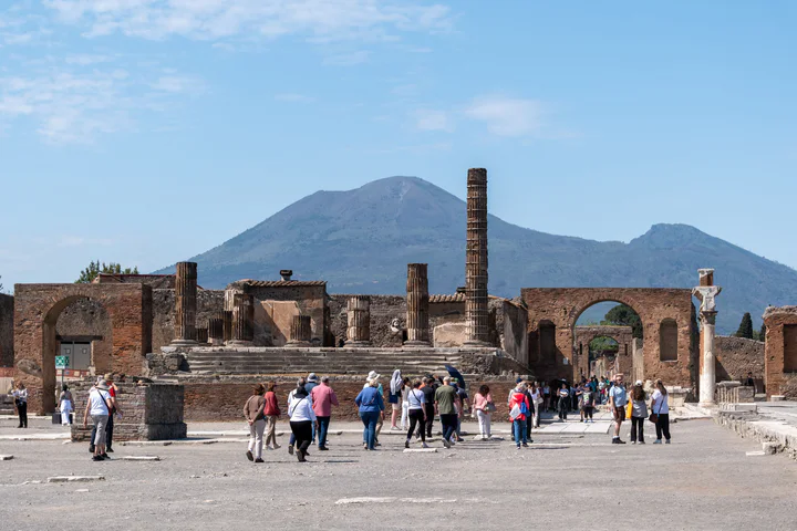 Ruins of arches, columns and buildings at the ancient Roman city Pompeii, with Mount Vesuvius in the background.