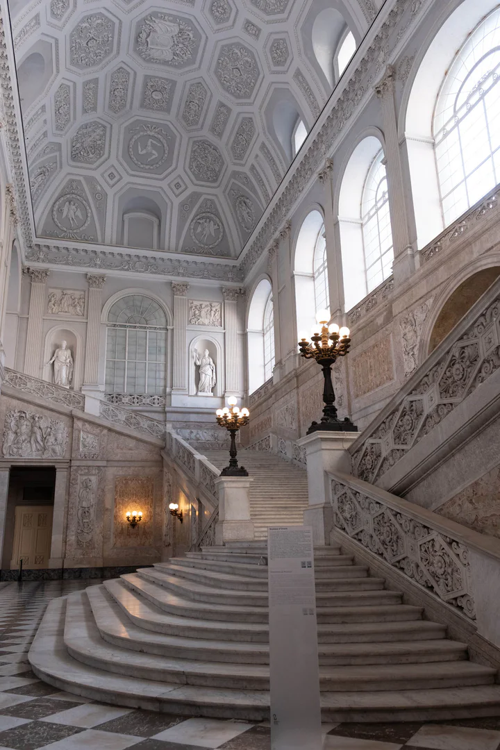 A beautiful white marble staircase in a grand, high-ceilinged room. It's all very ornate in shades of pale grey and cream.