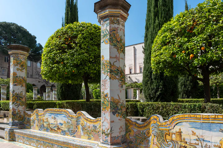 Painted, tiled columns and seats in blue, green and yellow in a church courtyard, with orange trees in the background.