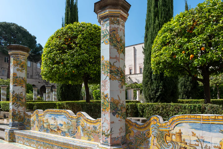 Painted, tiled columns and seats in blue, green and yellow in a church courtyard, with orange trees in the background.
