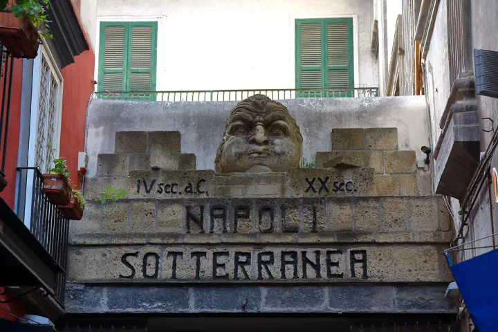 A stone entrance sign with a man's face making a blowing expression