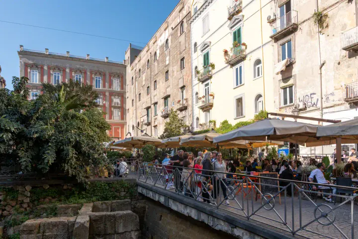 Piazza Bellini has an excavated section of the ancient Greek city walls in the middle of the square. The square is lined with bars.