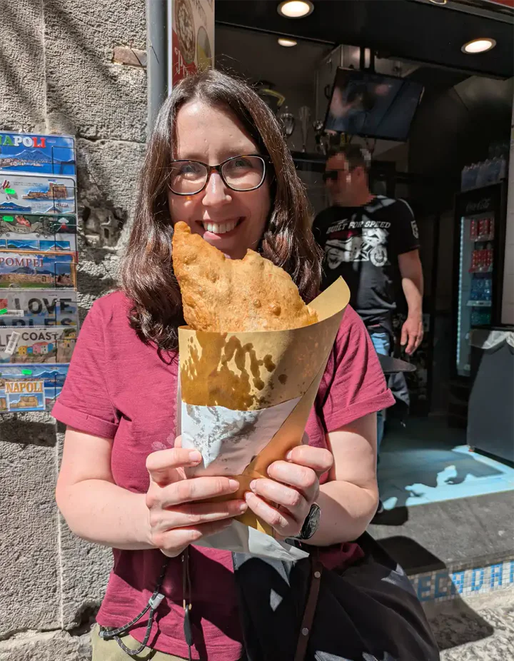 A woman with glasses holding a pizza fritta fried pizza. It's a semicircle shape and very large.