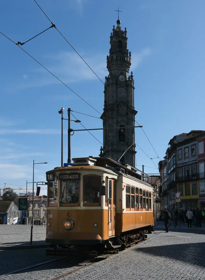 A vintage yellow Porto tram crossing the street in front of Clérigos Tower