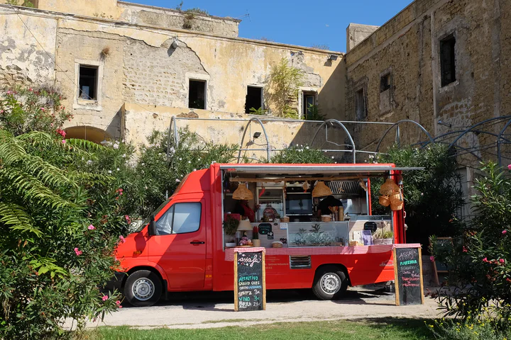 A cute red food truck parked in gardens outside a castle