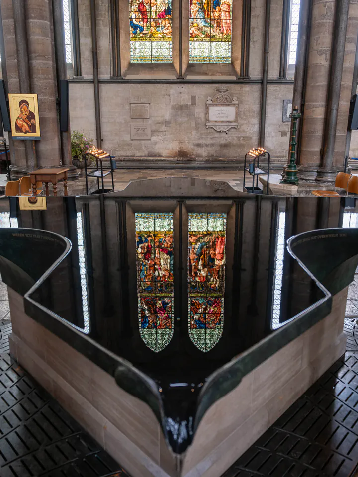 A large font with glassy black water, reflecting a stained glass window