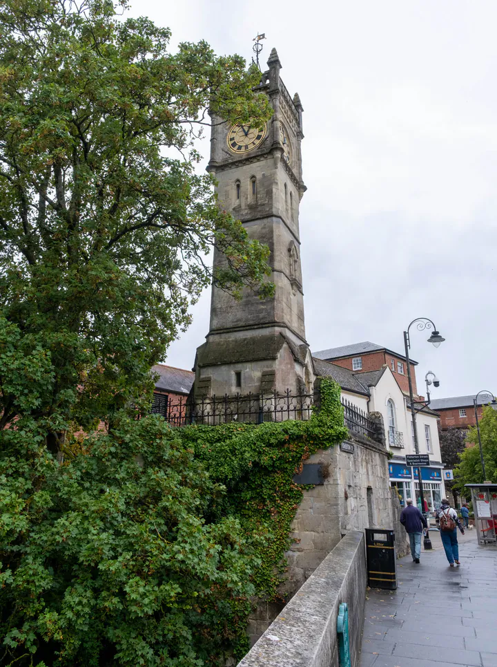 A tall, square, stone clock tower next to a bridge