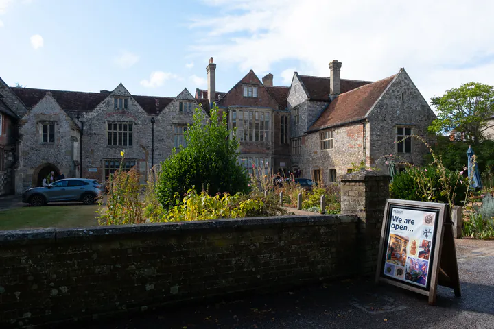 An old building with a pretty garden. A sign outside shows that the museum is open.