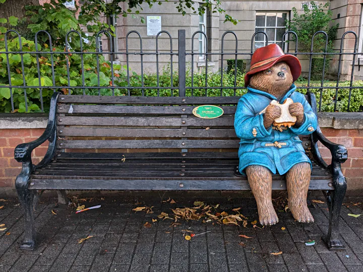 An ordinary bench with Paddington Bear sat on one end eating a marmalade sandwich