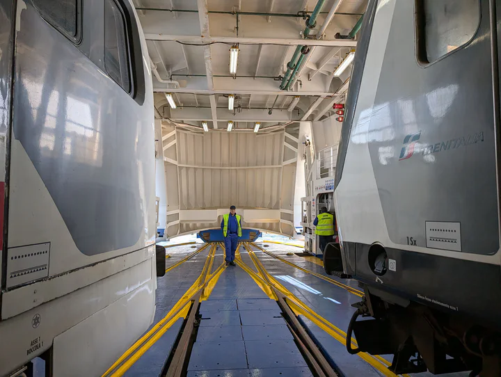 Two trains on a ferry; the ferry door is closing ready for the crossing.