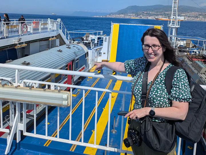 A woman carrying two bags and a camera on the deck of a ship