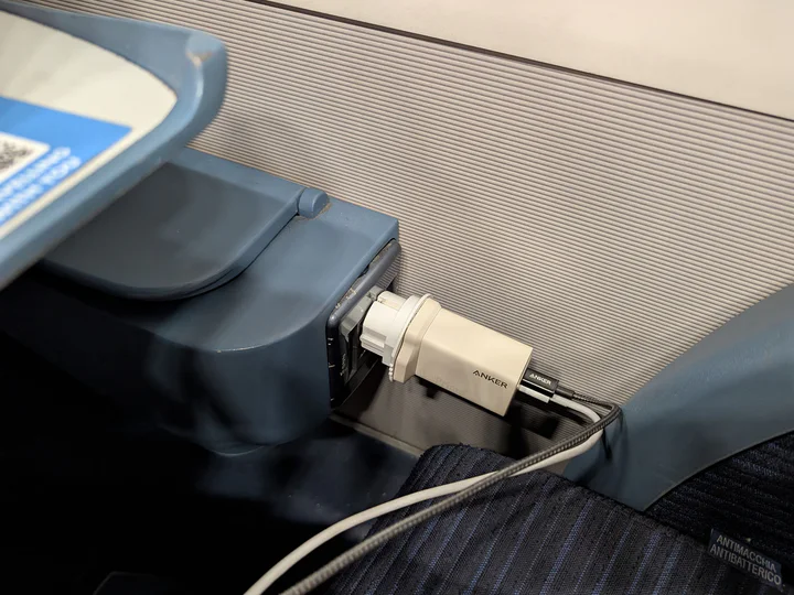 A plug socket on a train with a power adaptor just about hanging on in there