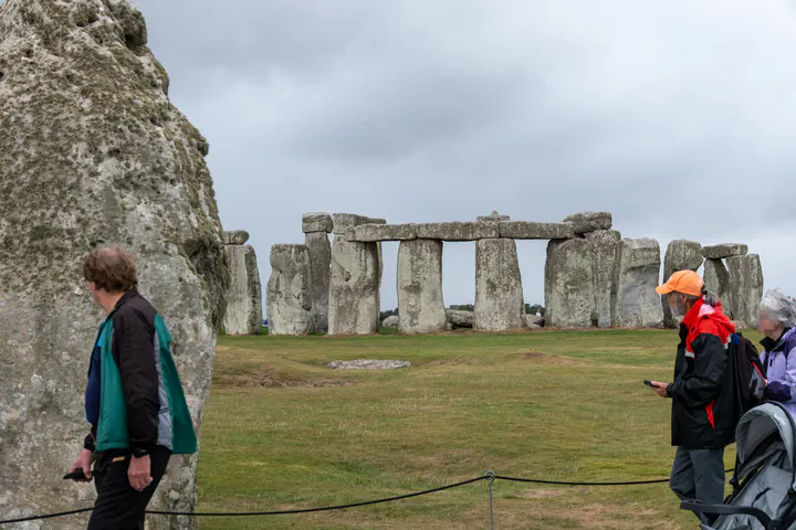A zoomed-in photo taken from the free footpath showing Stonehenge. There are a few people in the way.